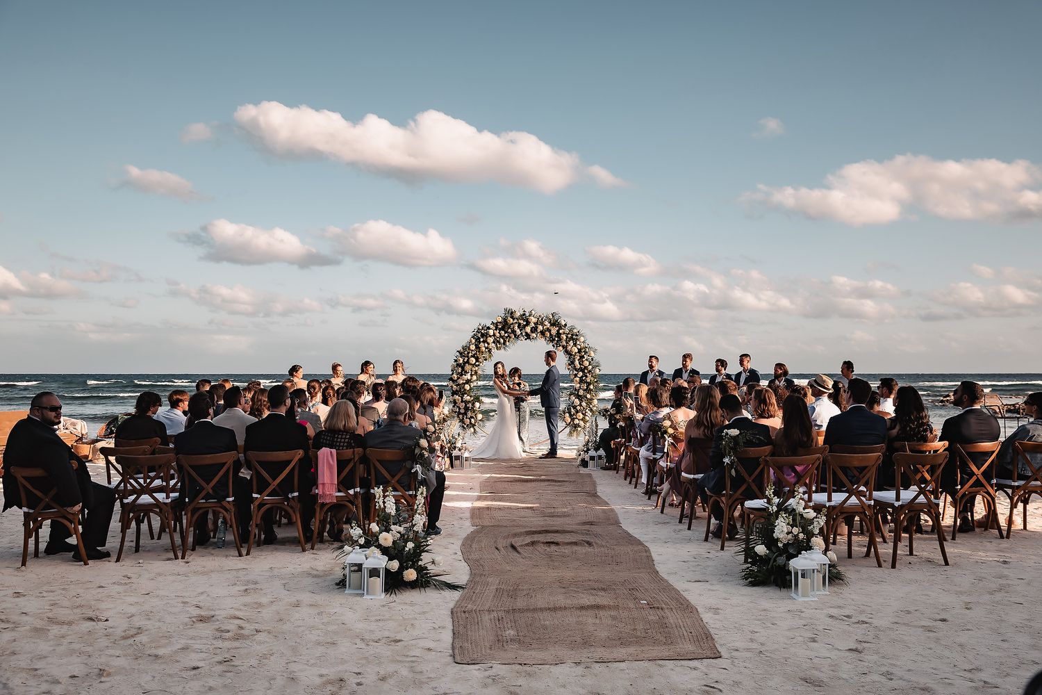 Panoramic view of a beach wedding ceremony with guests seated in rows facing the ocean.