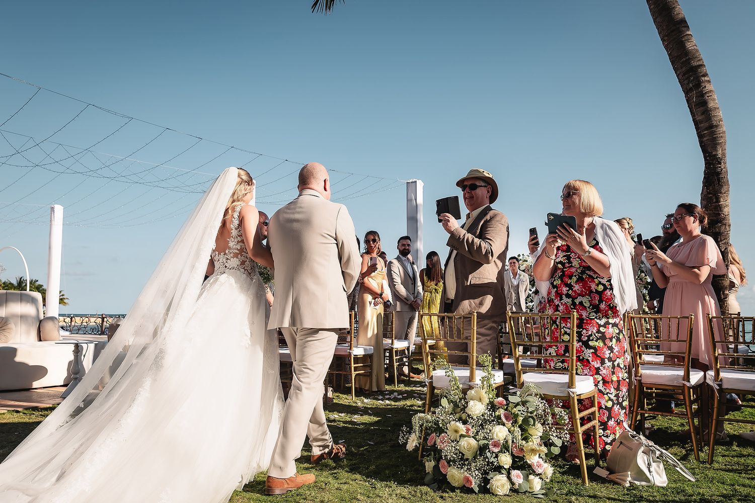 Outdoor wedding ceremony setup with white chairs and floral arrangements by the ocean.