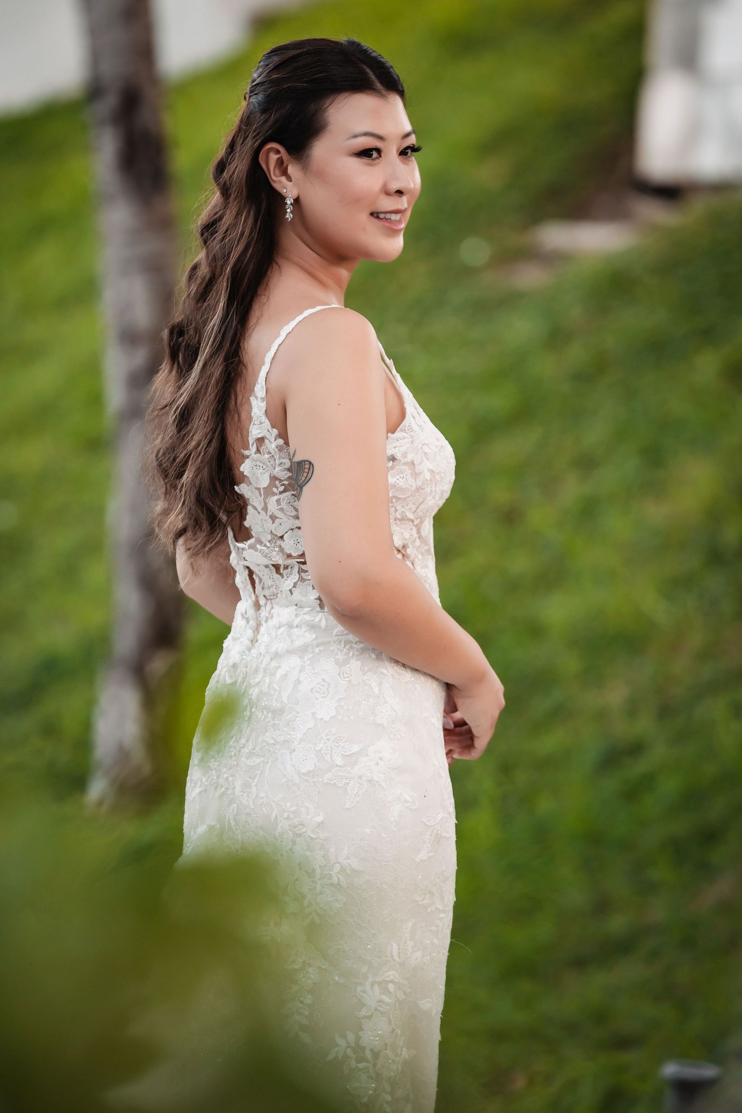 A beautiful bride in a lace wedding dress poses outdoors in a natural setting with greenery.