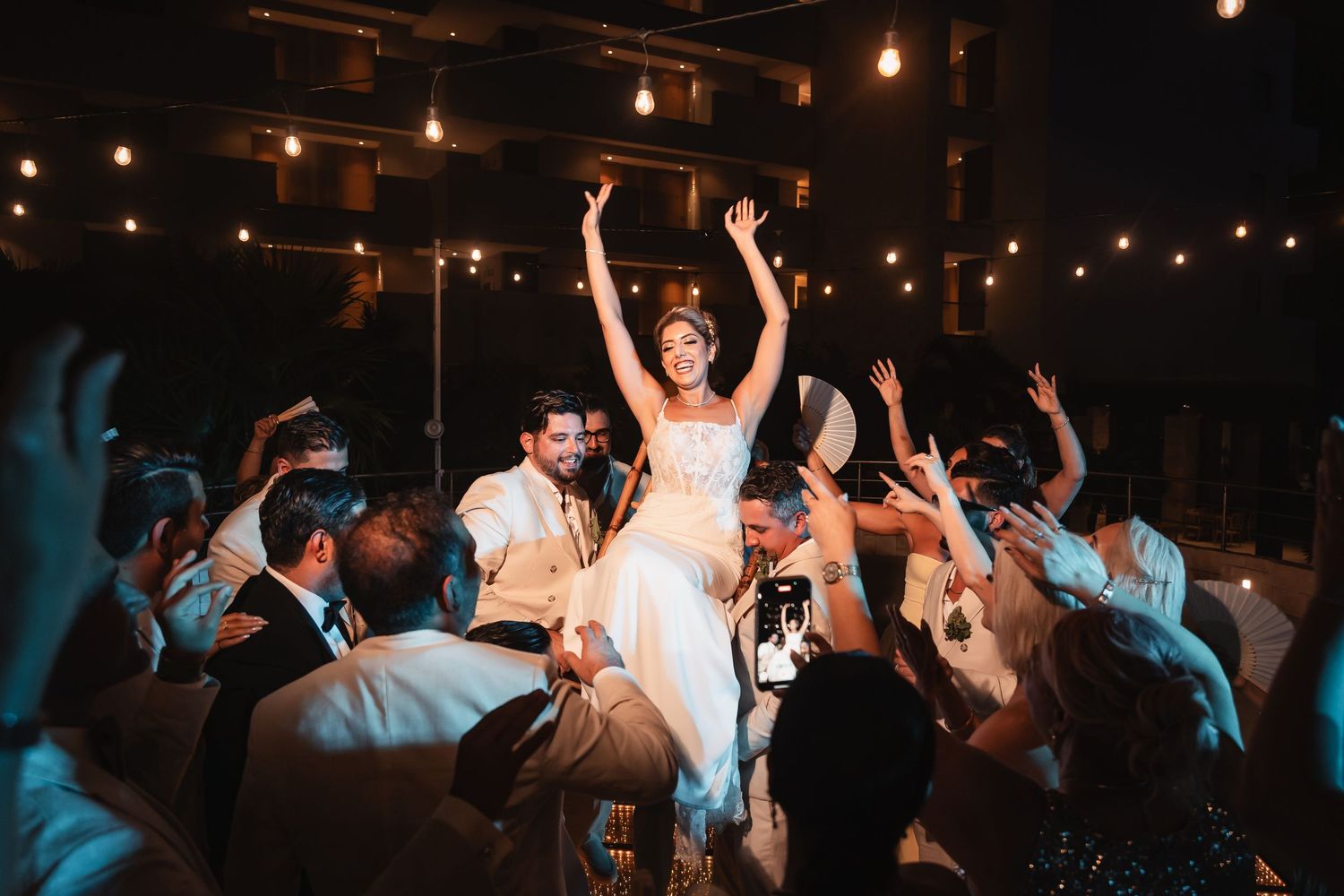 Dance floor filled with celebration under moody lighting and string lights at evening event.