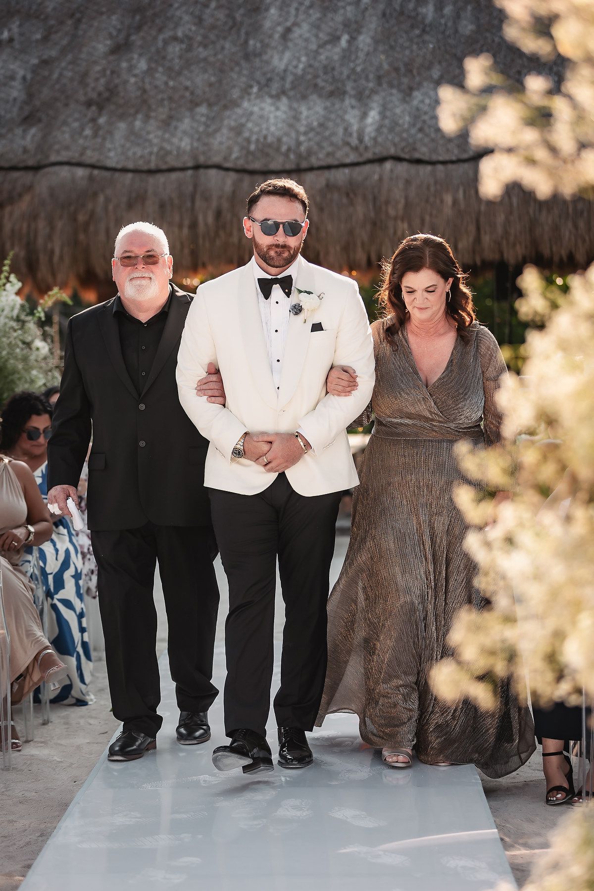 Wedding guests walking together on a white aisle runner at beach ceremony.