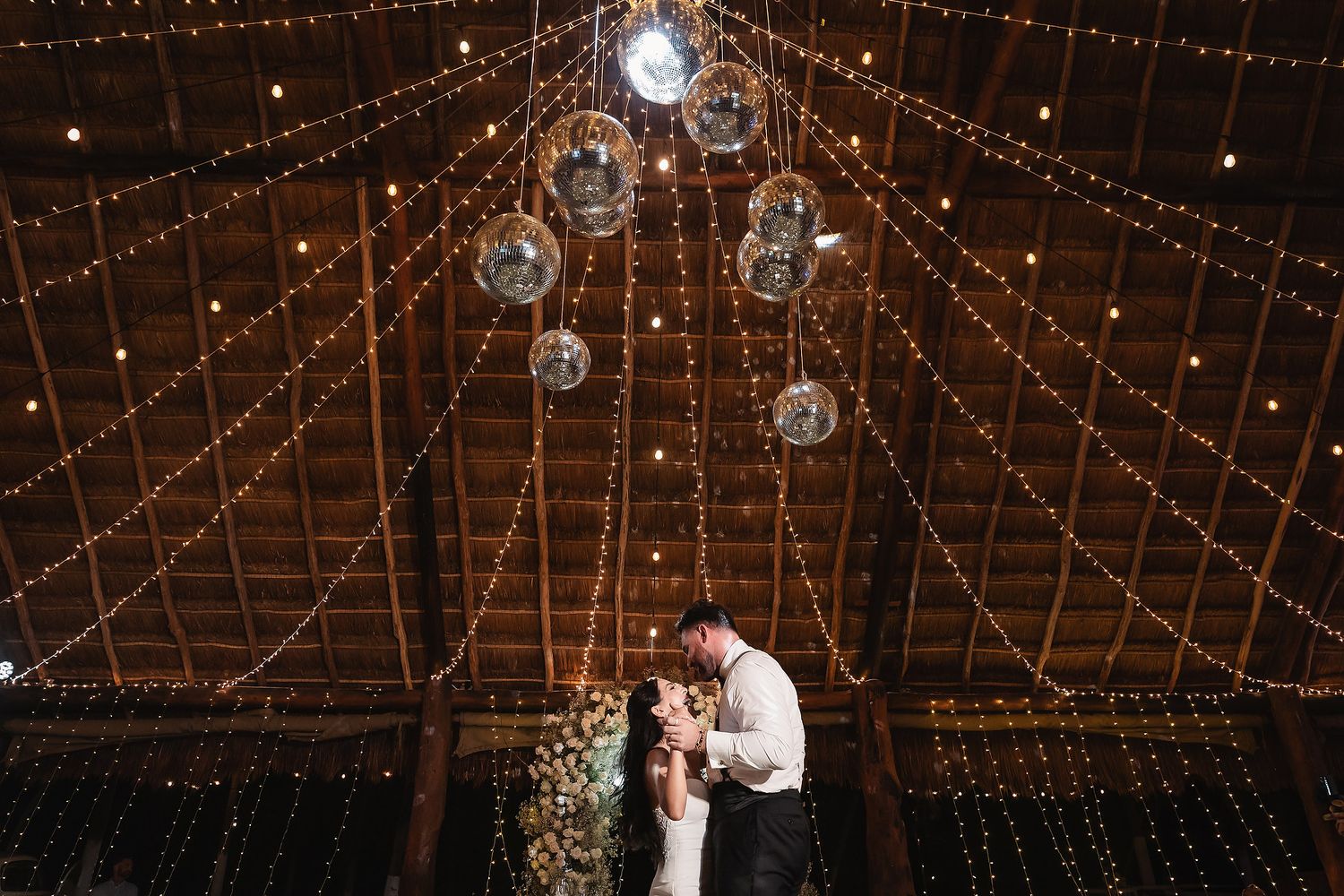 A romantic dance moment under strings of fairy lights and hanging disco balls in a wooden barn.