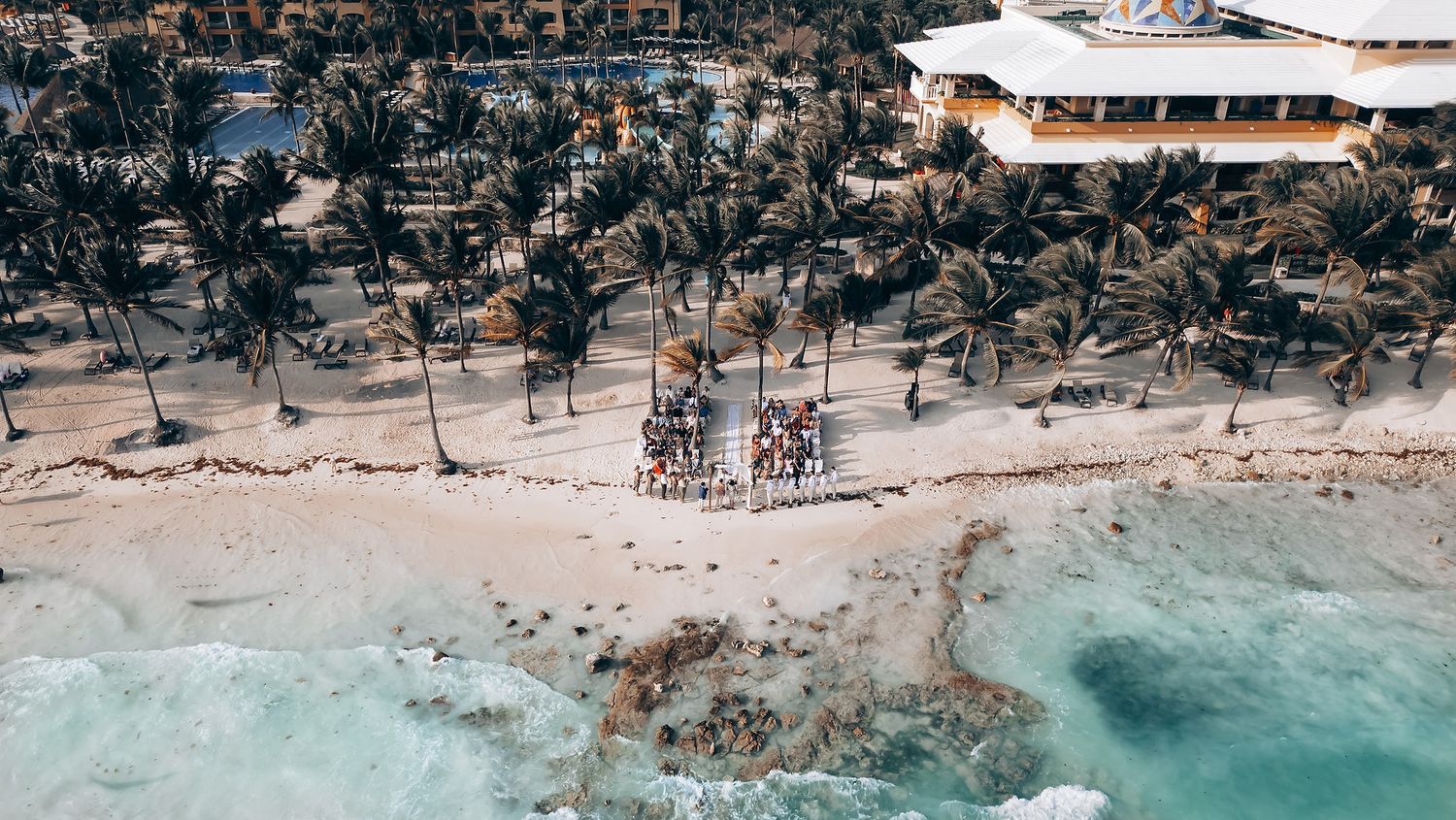 Aerial view of a tropical beach wedding venue with turquoise waters and palm trees.