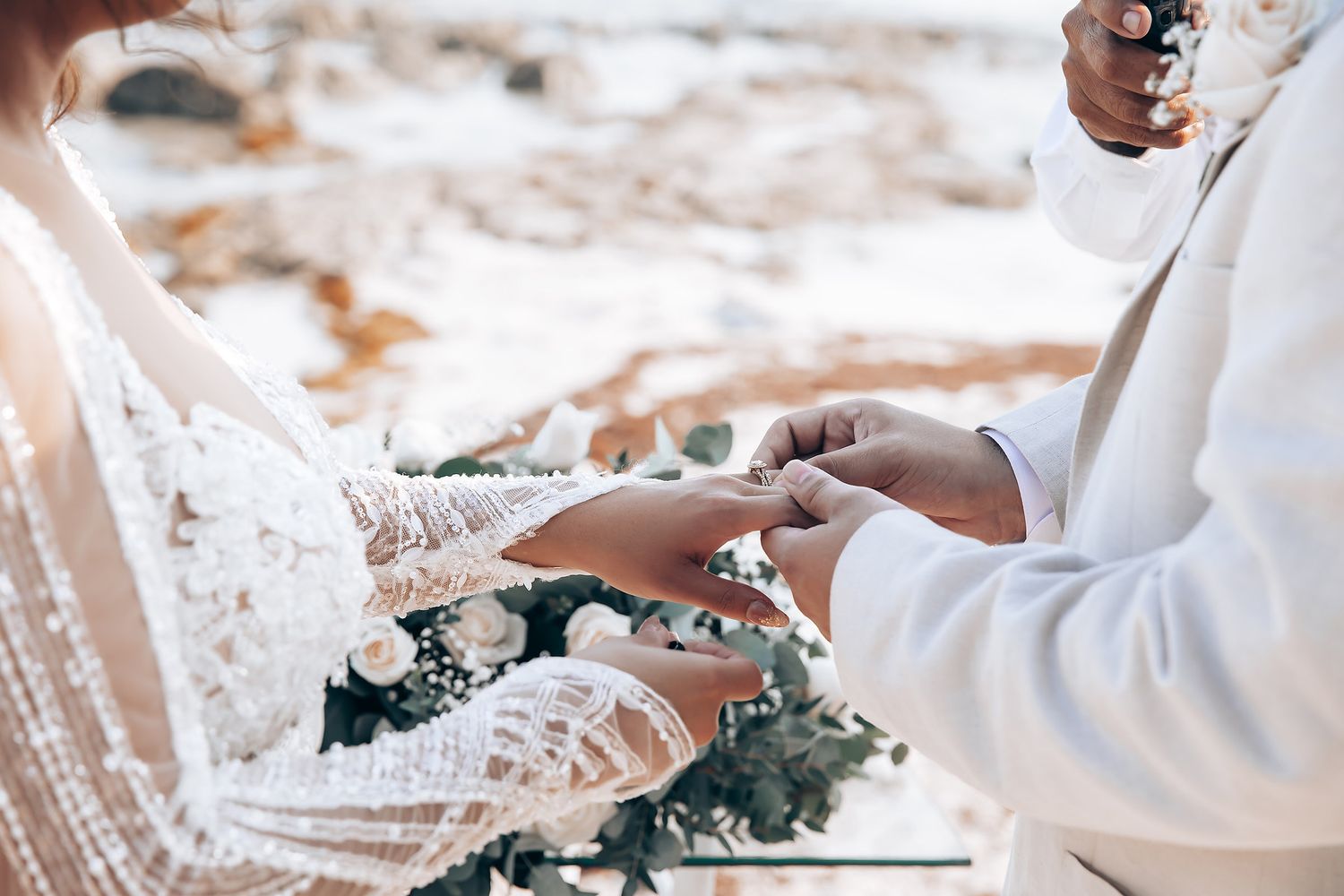 Close-up of hands exchanging wedding rings during beach ceremony with soft lighting.
