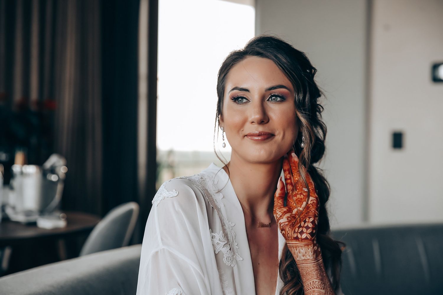 A woman in white robe with henna design on her hand sits in preparation for her wedding day.