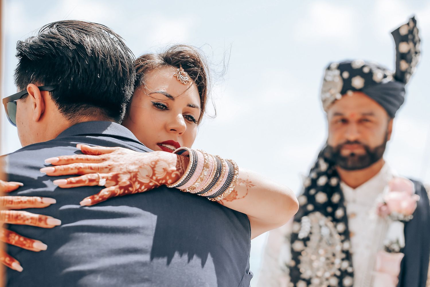 A wedding couple shares an intimate embrace during their outdoor ceremony while guests look on.