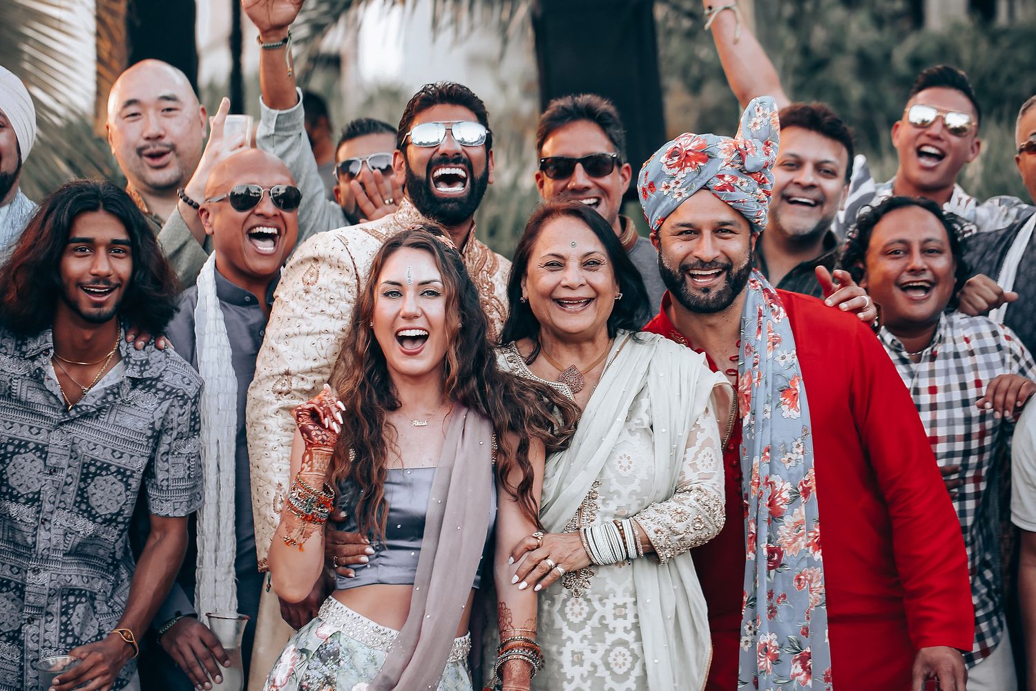 Large group of wedding guests smiling and celebrating together outdoors in a candid group photo.