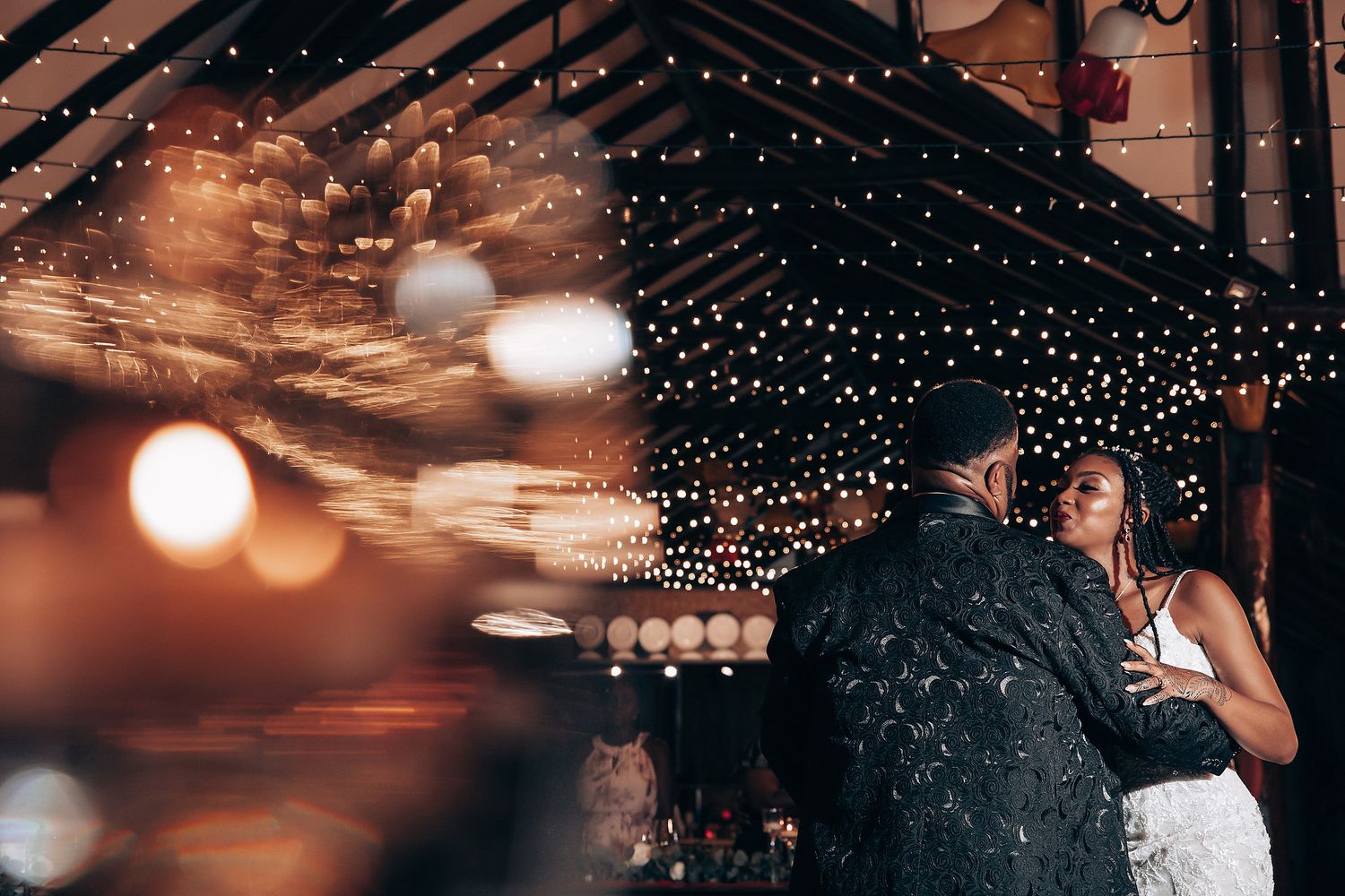 A couple dances under twinkling string lights at a romantic evening reception.
