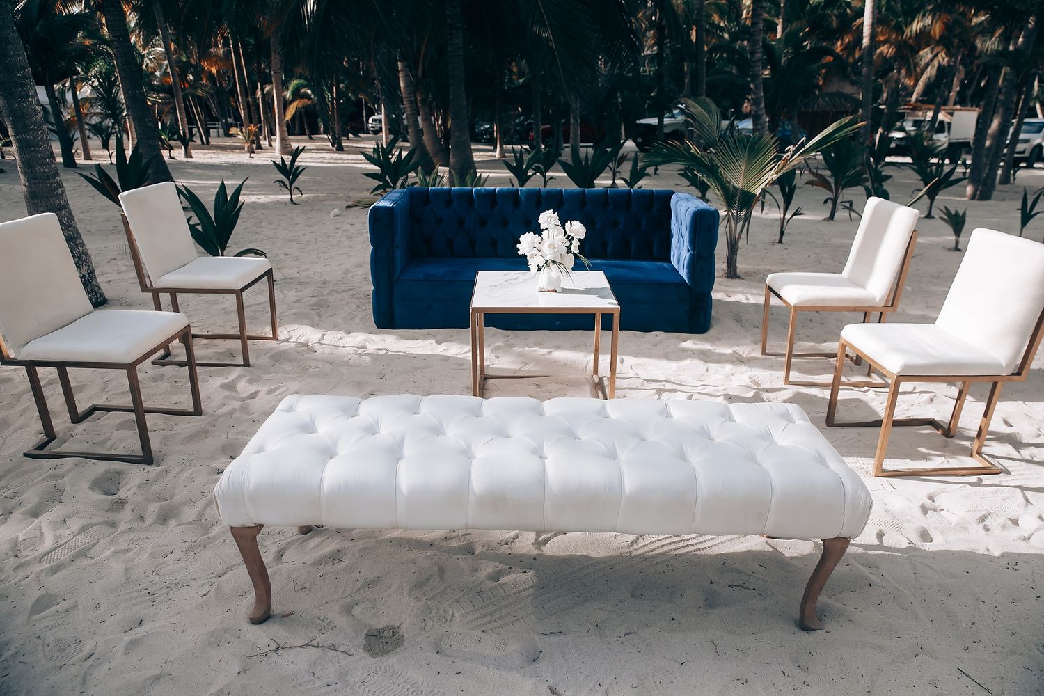 Modern wedding reception setup with white lounge furniture and wooden accents in an outdoor venue.