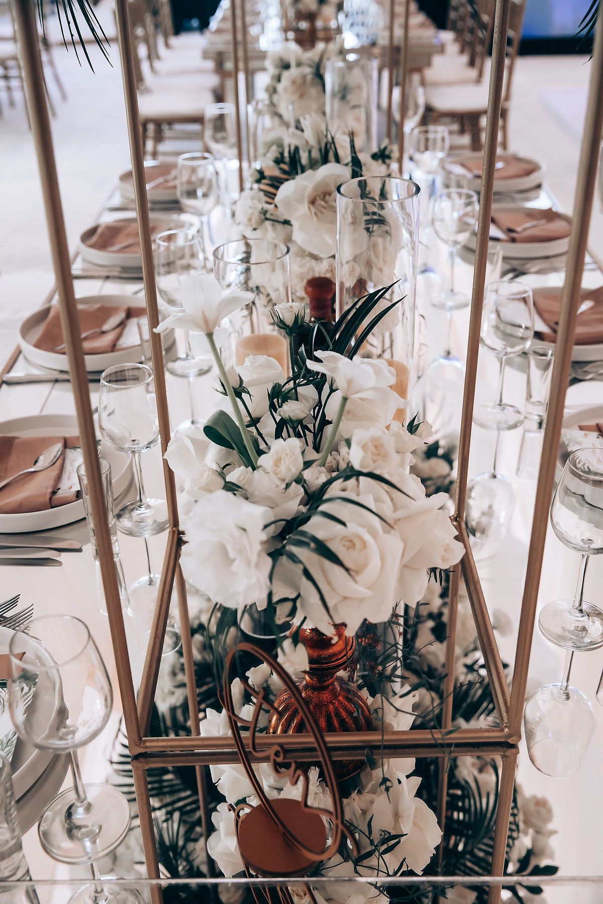 Elegant wedding table setting with white floral centerpieces and glass decor arranged in geometric frames.