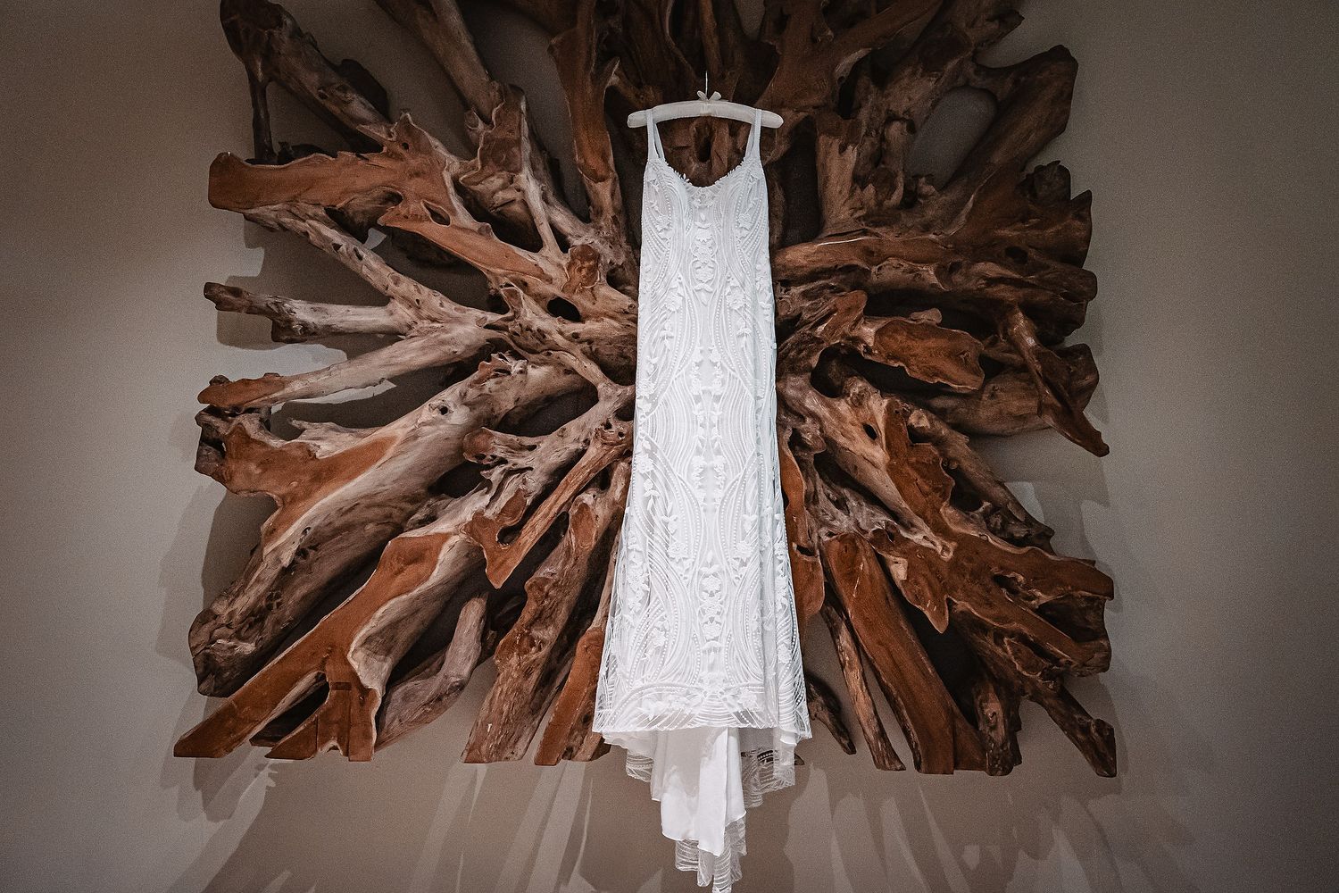 Rustic driftwood chandelier hangs above with white wedding dress displayed in soft lighting.