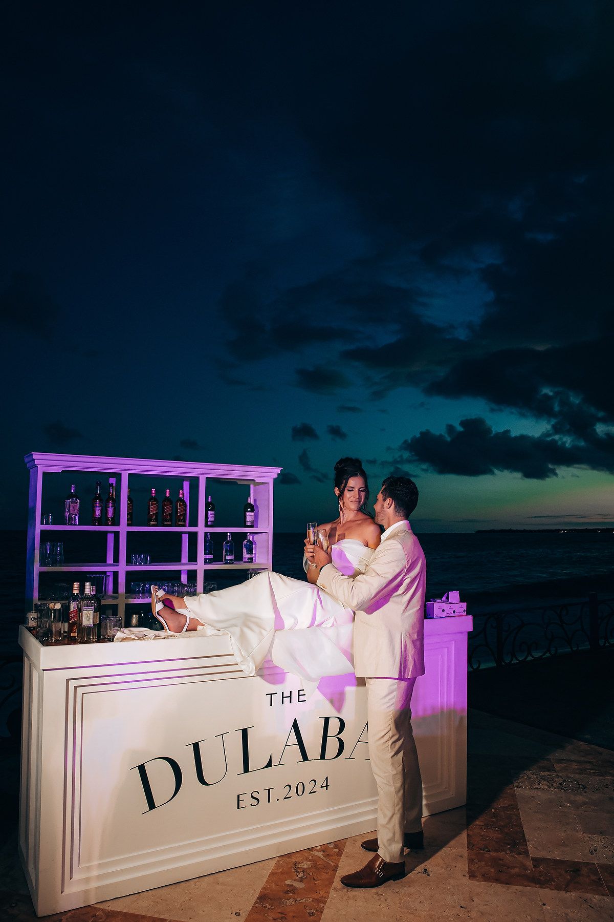 Illuminated wedding bar setup with purple lighting against a dark evening sky.