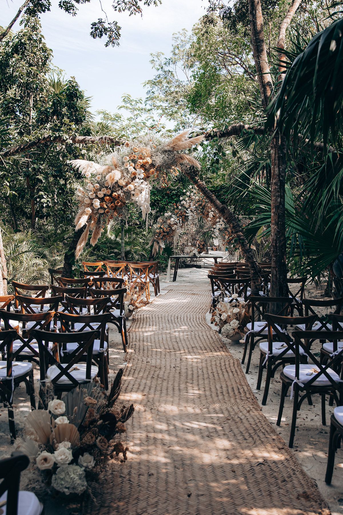 Wedding ceremony setup with black cross-back chairs and floral arrangements along a brick pathway.