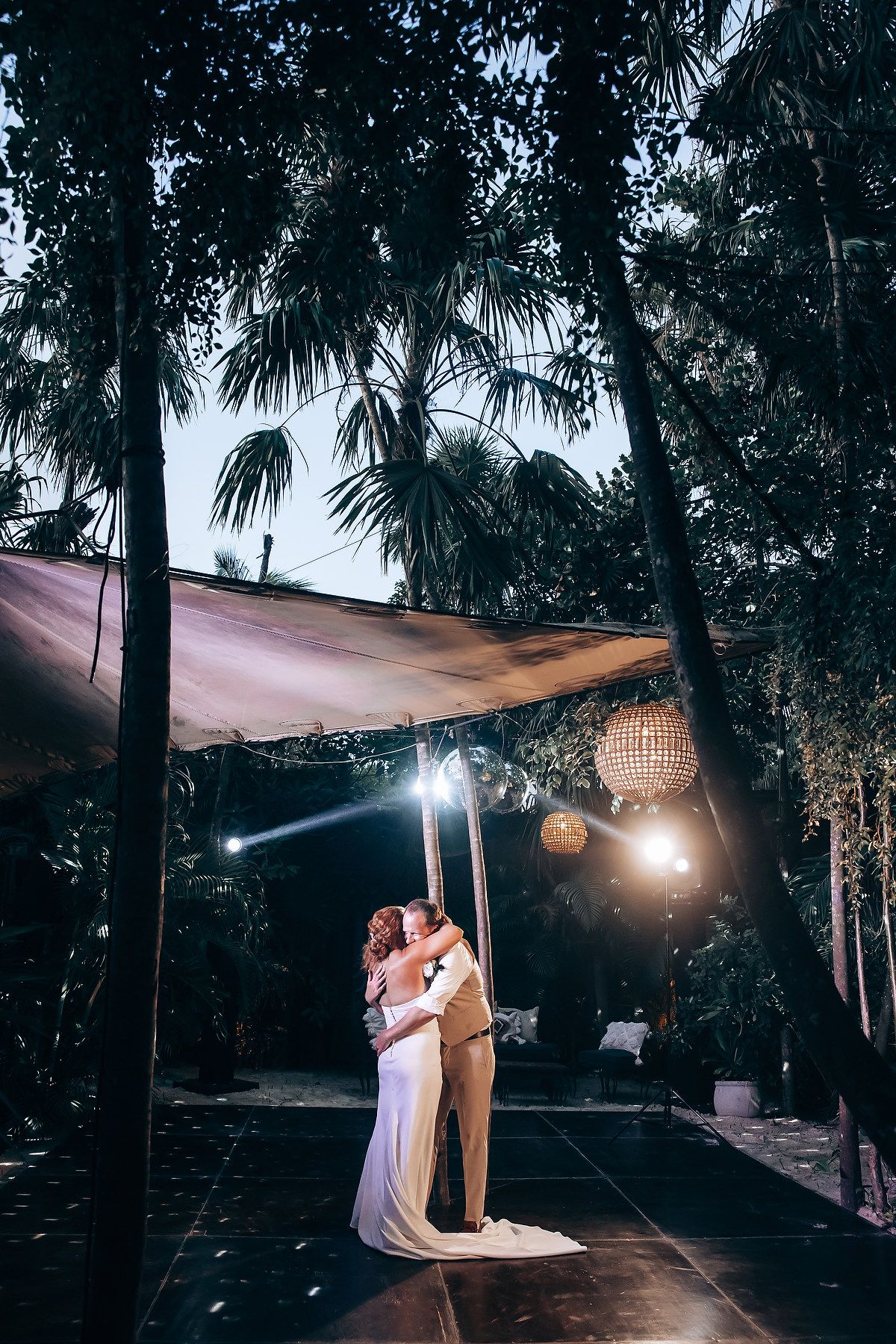 Couple sharing their first dance under elegant chandeliers and draped outdoor canopy.