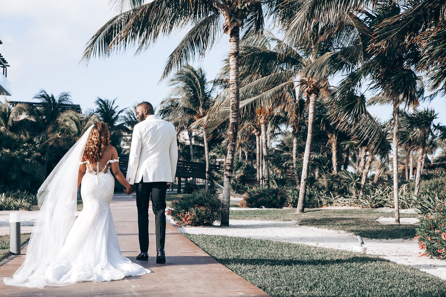 A couple takes wedding photos on a tropical path lined with palm trees.