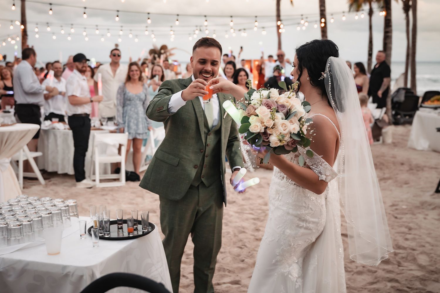 Wedding celebration on a beach with string lights and floral arrangements.