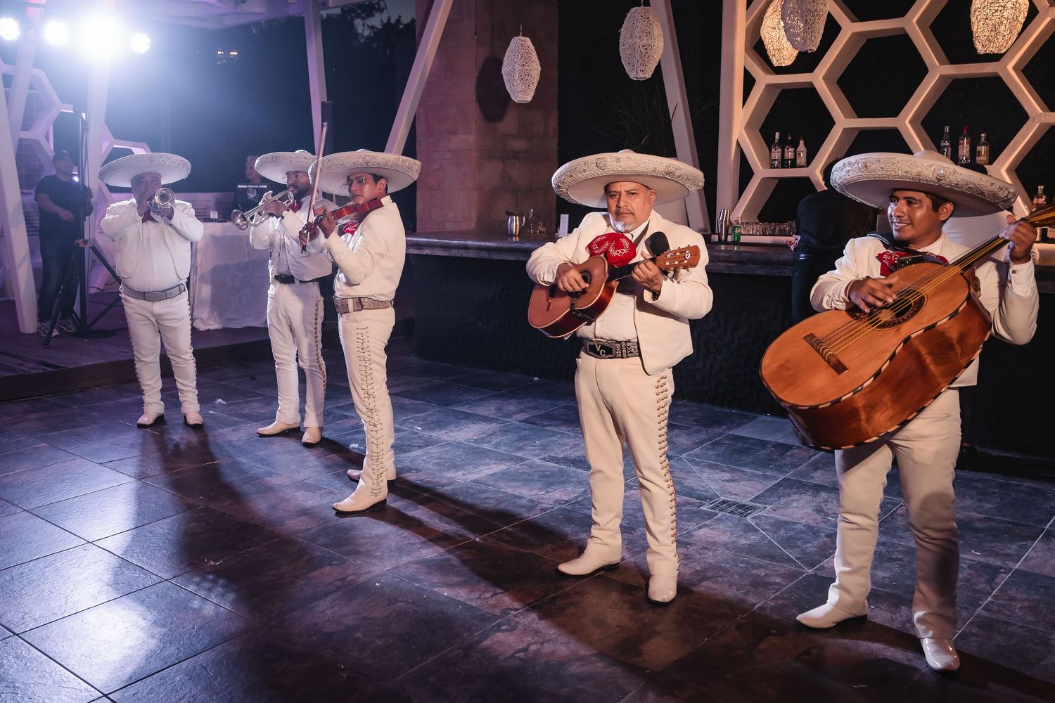 Wedding reception performers in white outfits dance on illuminated stage with geometric backdrop.
