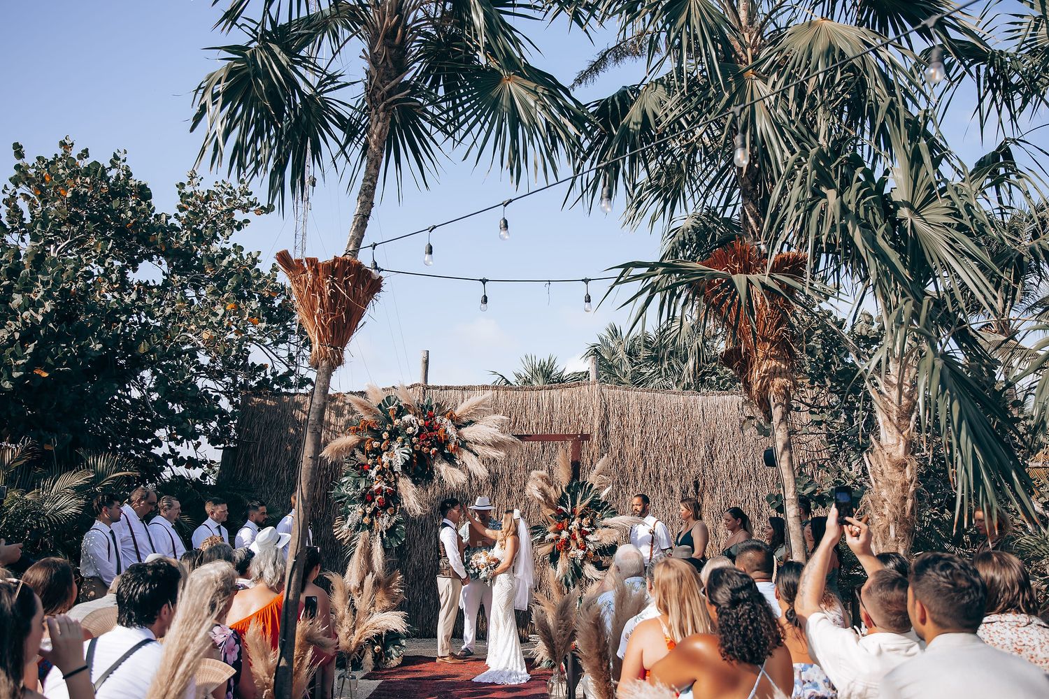 Outdoor wedding party with tropical decor and string lighting creating a magical atmosphere.