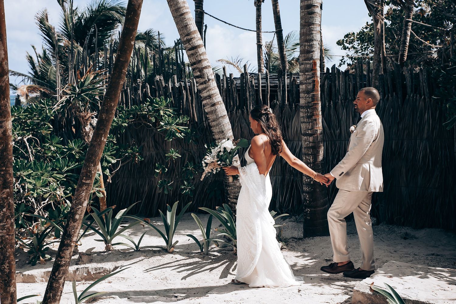 Beach wedding ceremony setup with palm trees and natural decor on white sand.