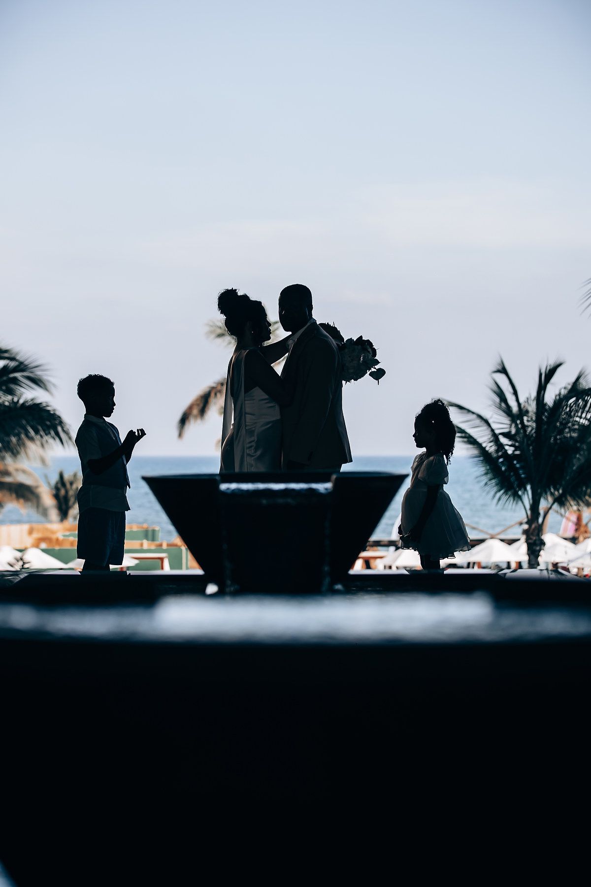 Silhouettes of people gathered outdoors against a sunset sky with palm trees in the background.