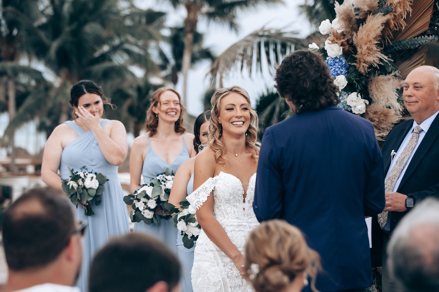 A beachside wedding ceremony with bridesmaids in light blue dresses and tropical floral decorations.