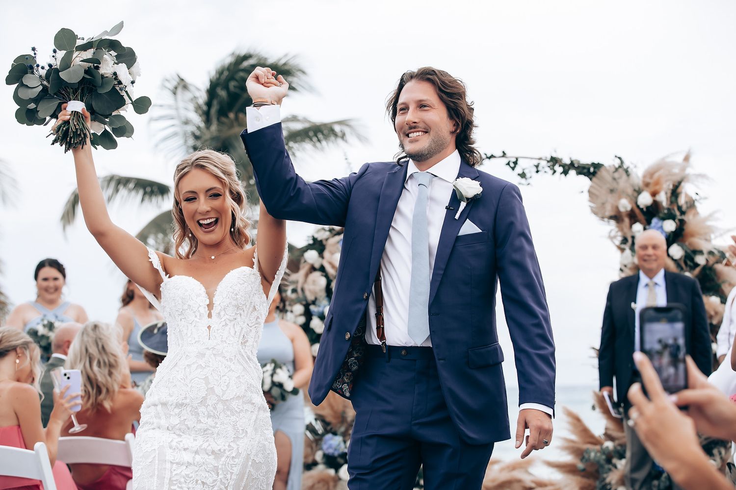 Joyful wedding celebration with bridal party on a wooden deck by the ocean.