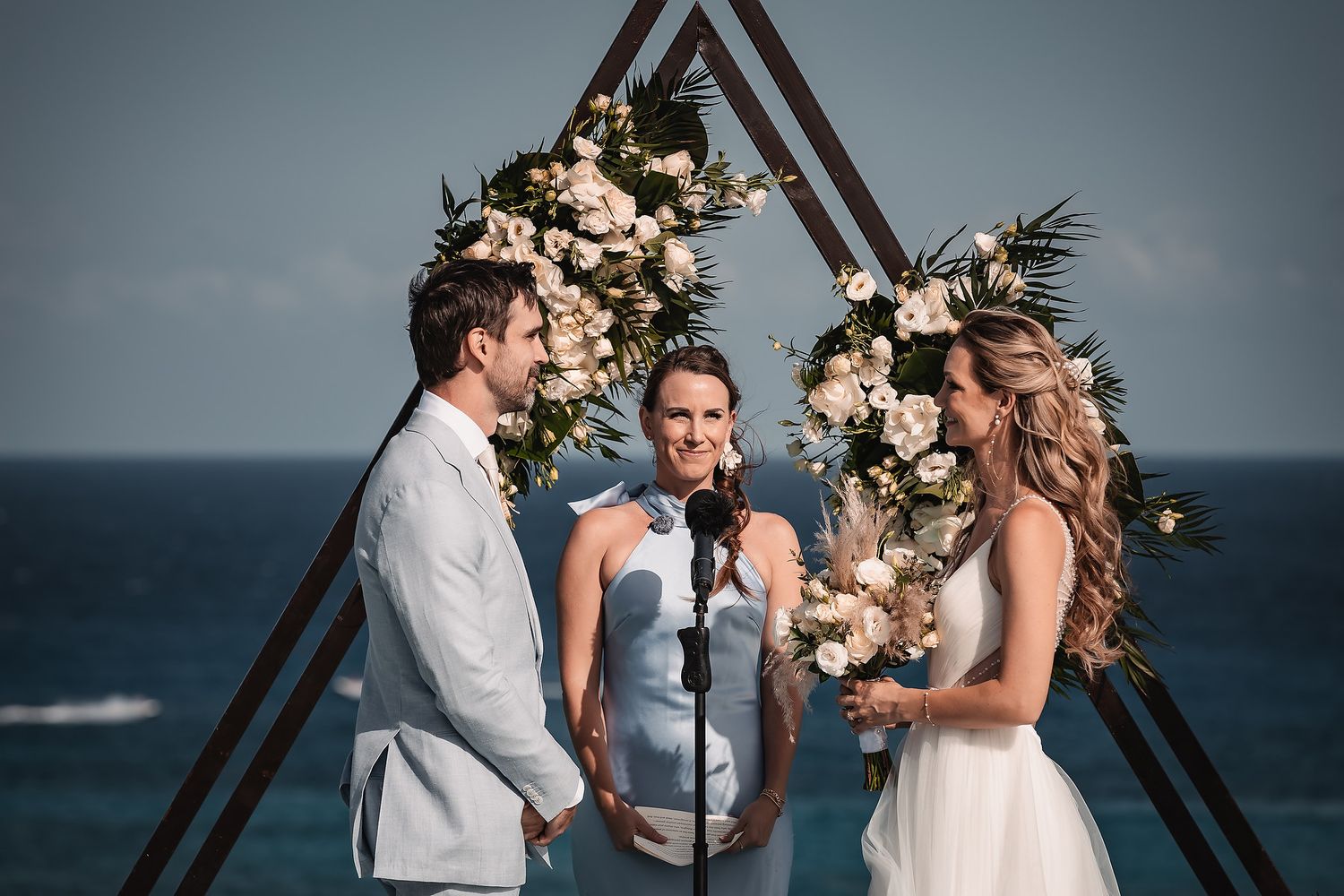 Intimate beach wedding ceremony with geometric arch and romantic floral decorations.