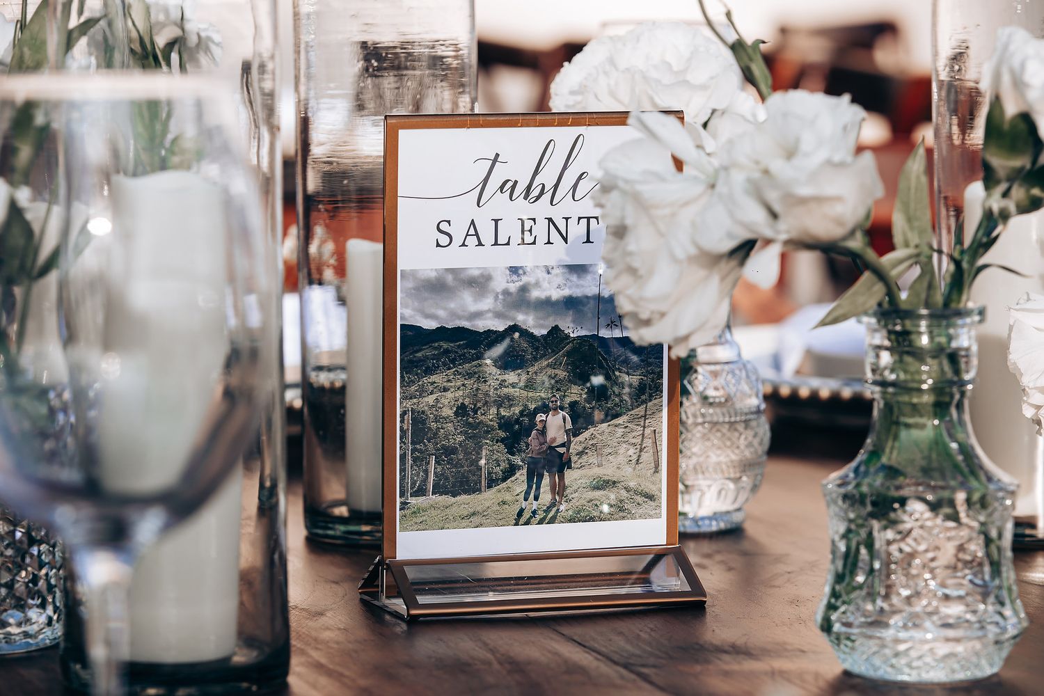 Wedding reception table decor with elegant glassware, floral arrangements, and table number displays in a rustic setting.
