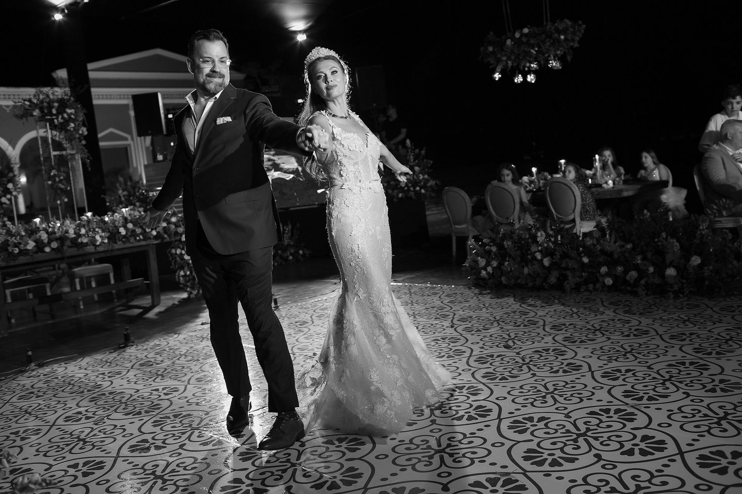 Couple dancing together at an elegant wedding reception on a patterned dance floor.