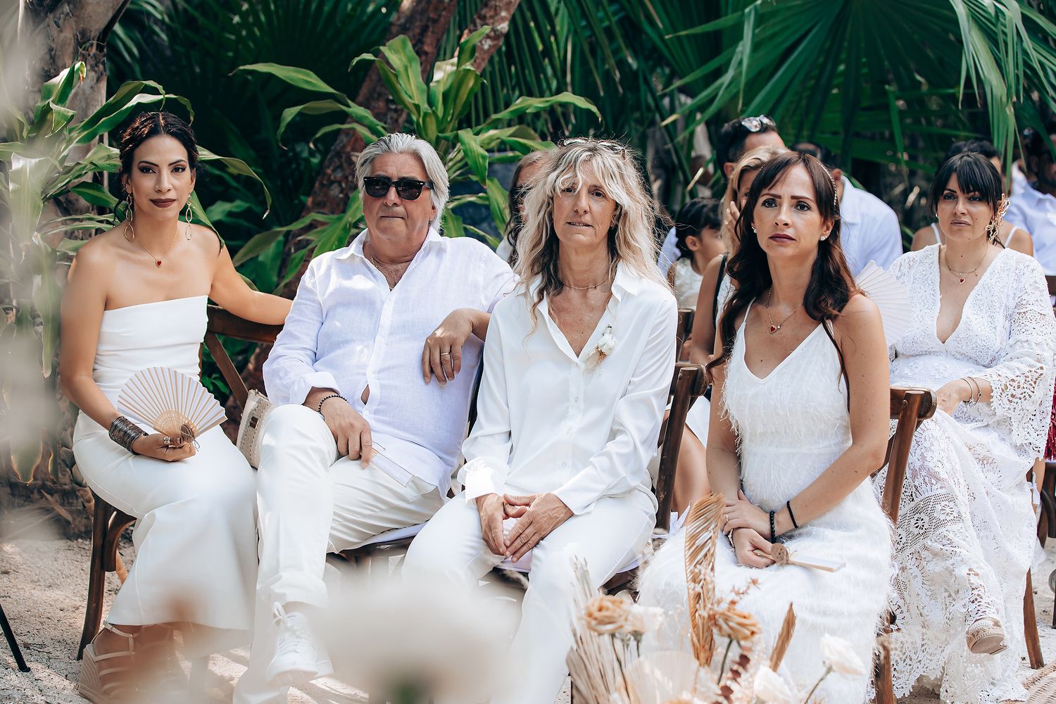 Wedding party dressed in white poses together in a tropical garden setting for formal group photos.