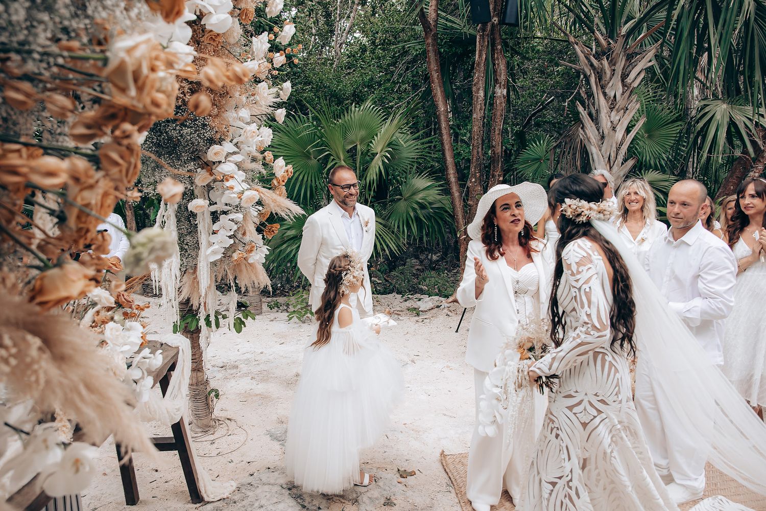 A group in white dresses poses together in a lush garden setting for a wedding photo session.