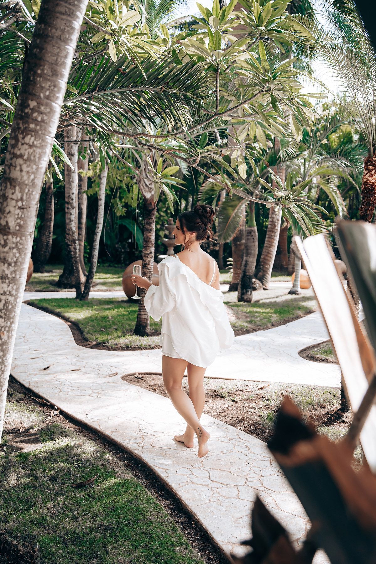 A stone walkway meanders through a serene palm grove with filtered sunlight creating dappled shadows.