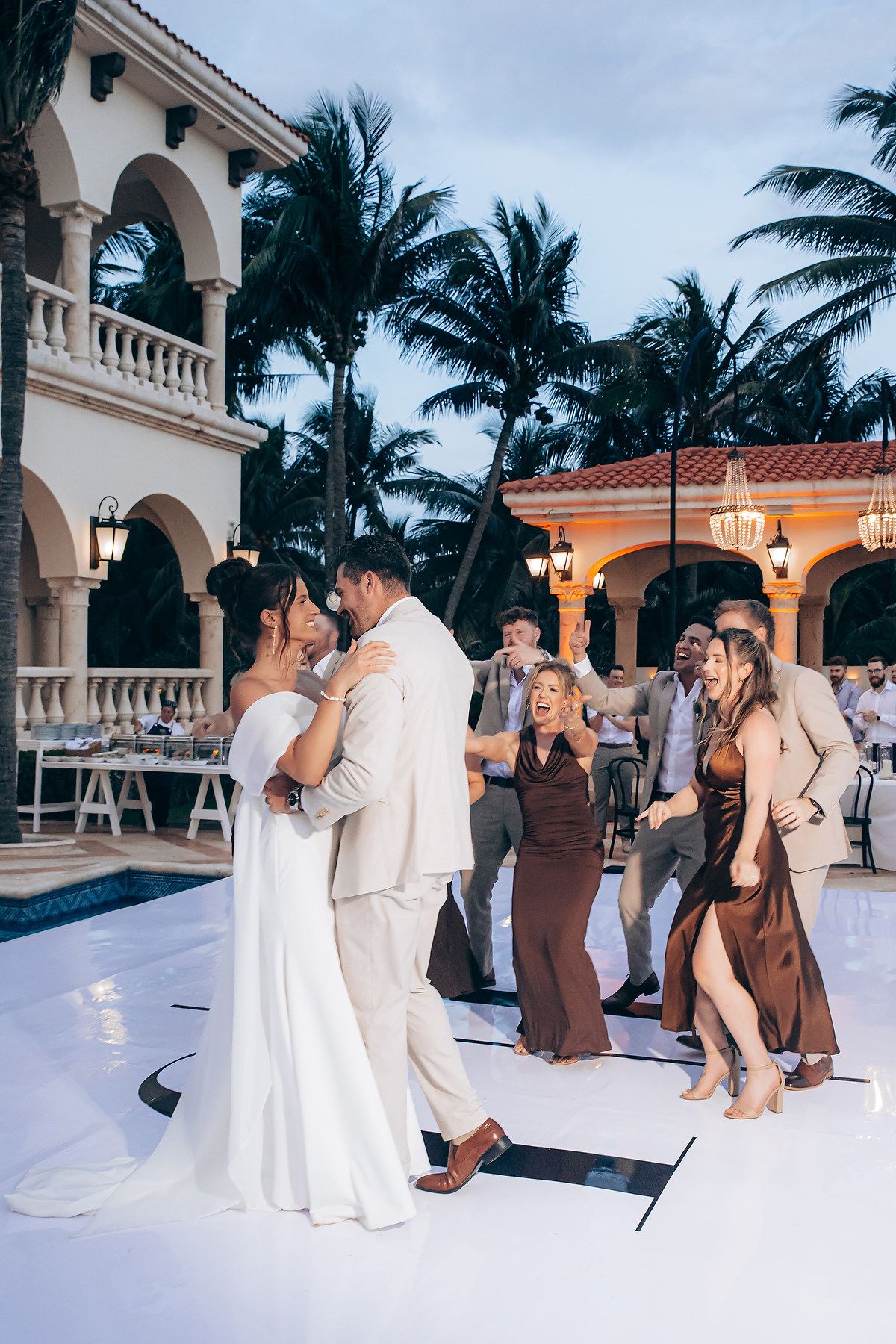 Wedding party performs a synchronized dance routine on an elegant outdoor terrace with palm trees in the background.