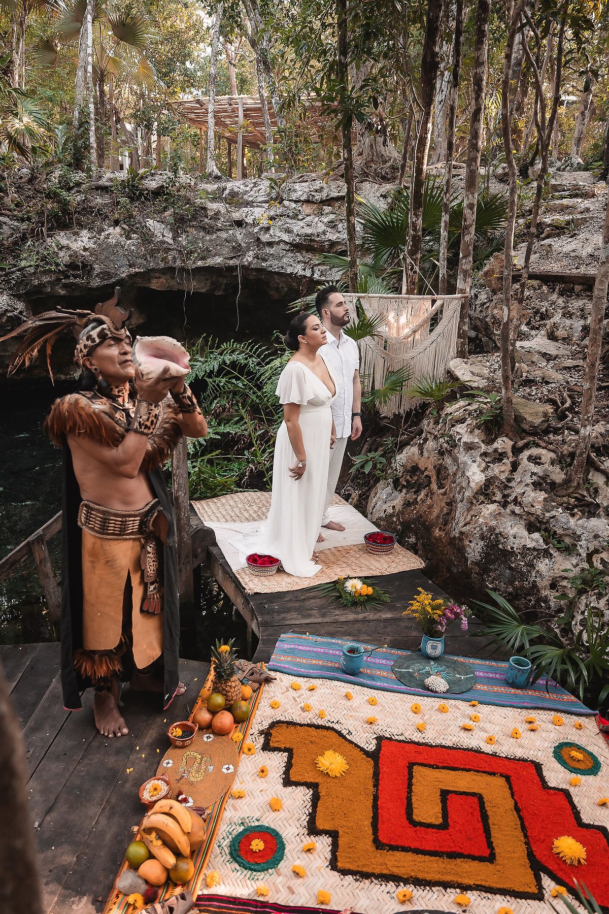 Mayan wedding ceremony on wooden platform with colorful traditional rug and ceremonial offerings.