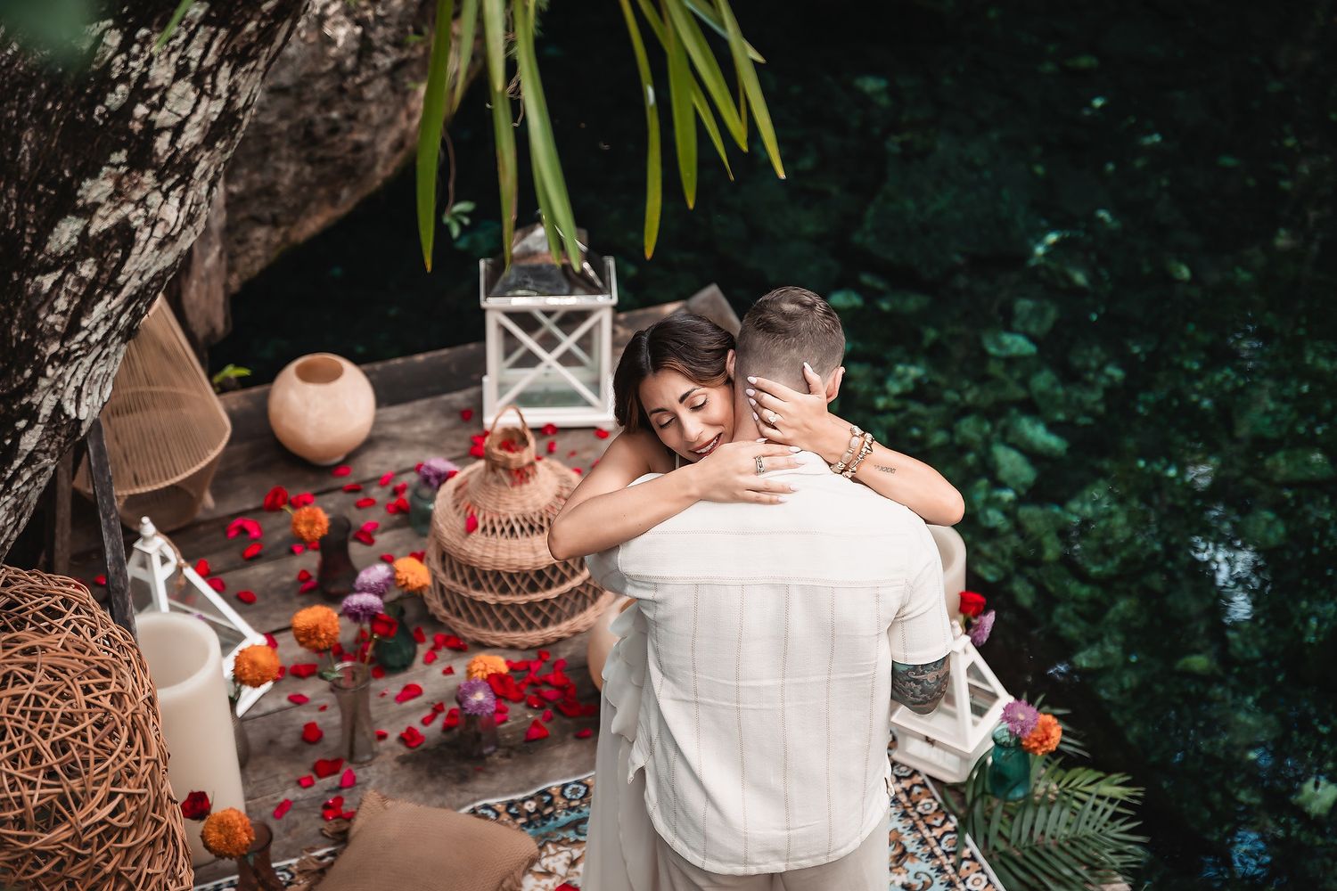 Intimate moment by turquoise cenote waters with decorative lanterns and flowers.
