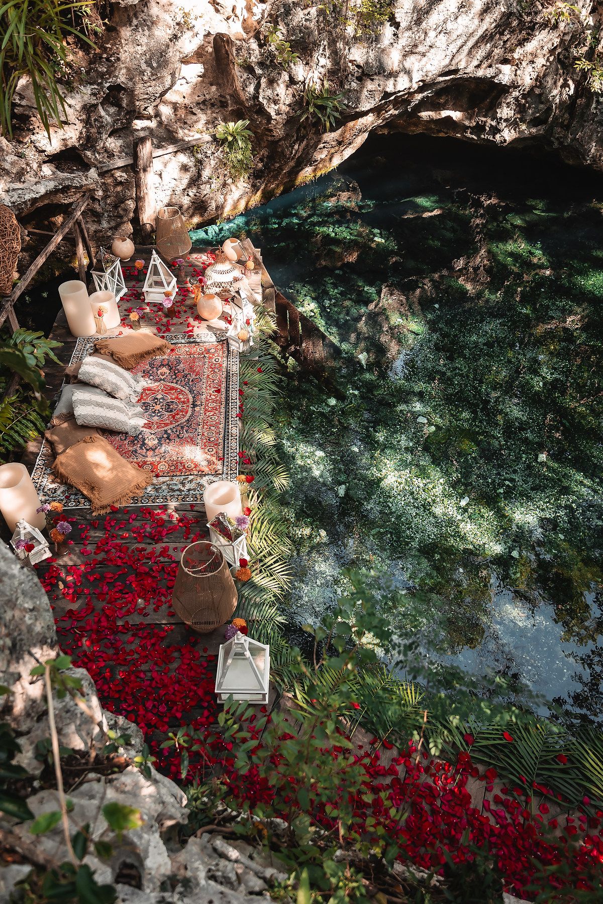 Ornate picnic display with Persian rugs and lanterns beside turquoise cenote waters.