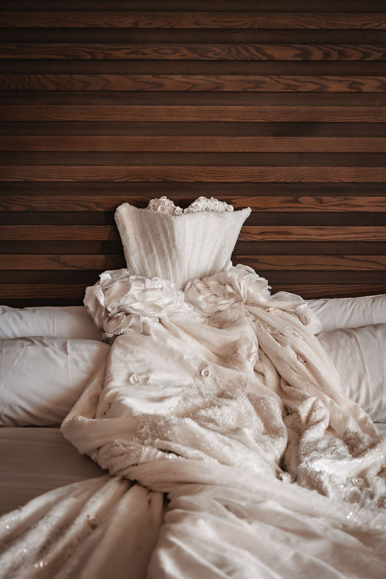 Detail shot of a white wedding dress with intricate lace laid out on dark wooden planks.