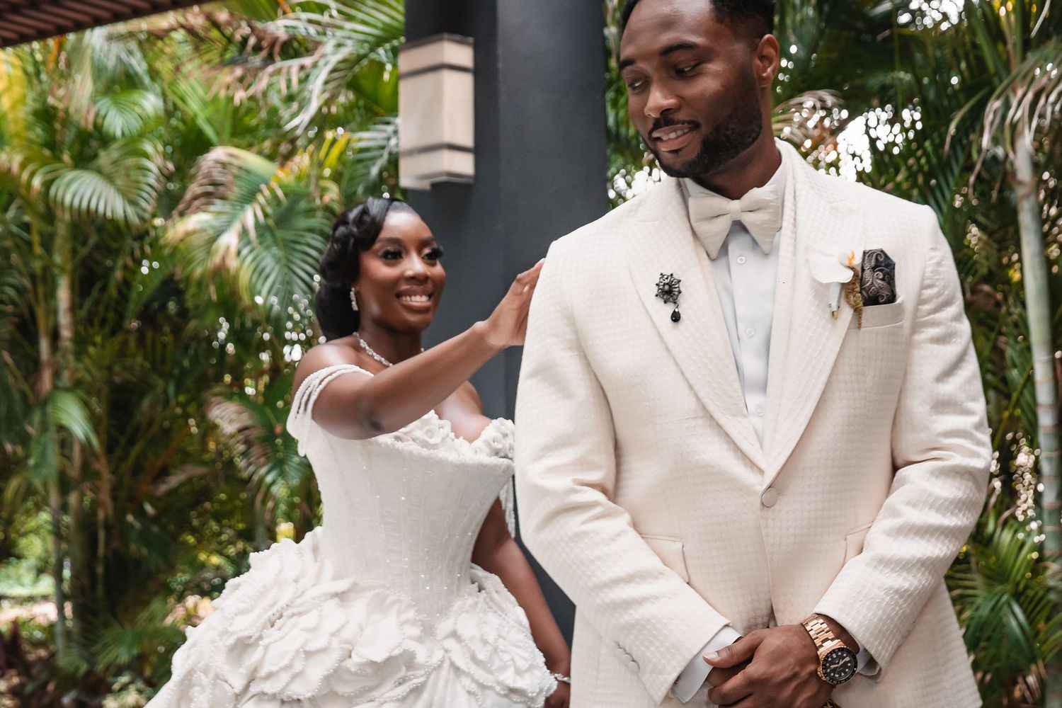 A wedding couple interacts playfully in a lush palm garden setting.