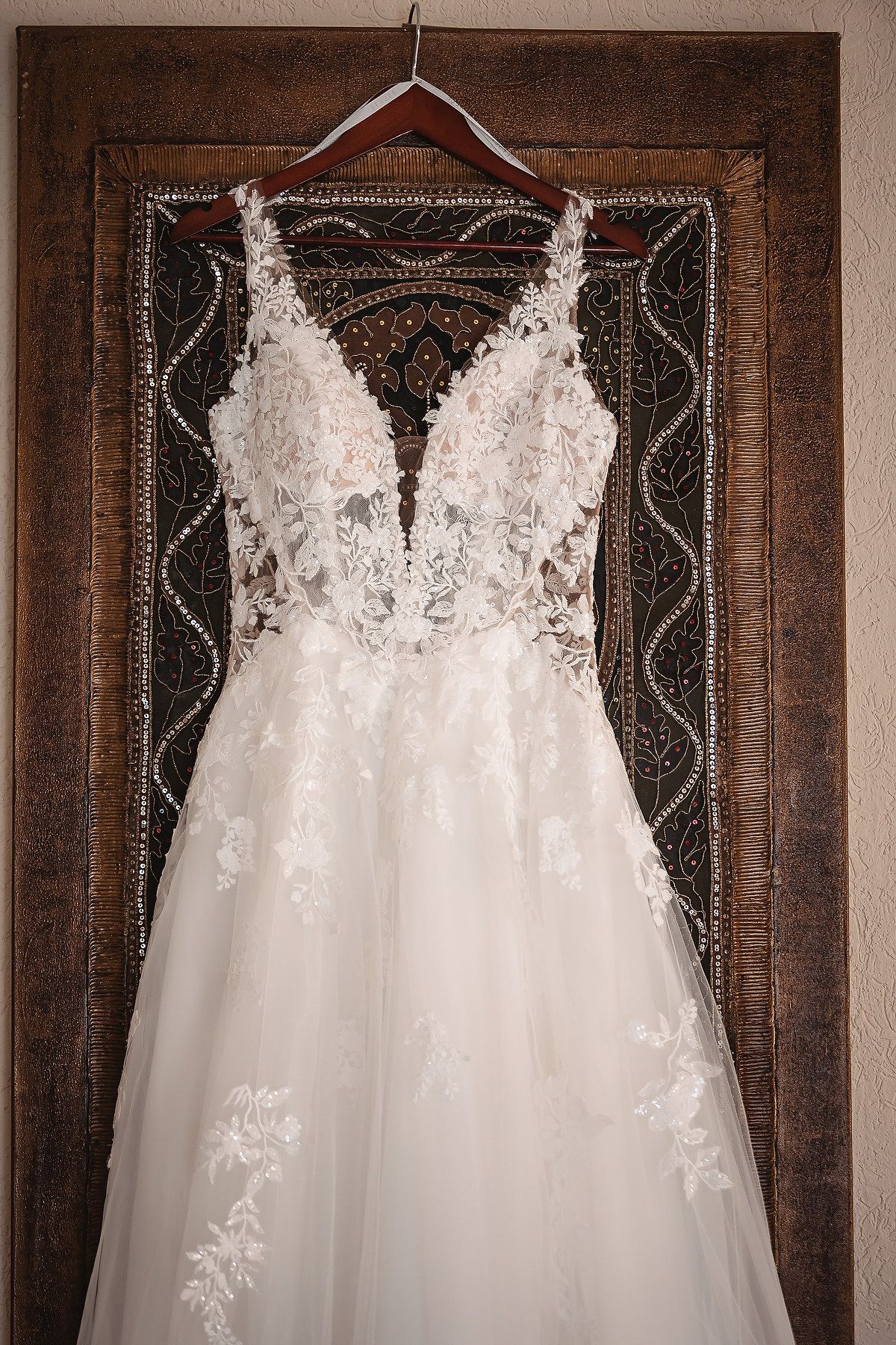 Elegant white lace wedding dress displayed against dark wooden panels.
