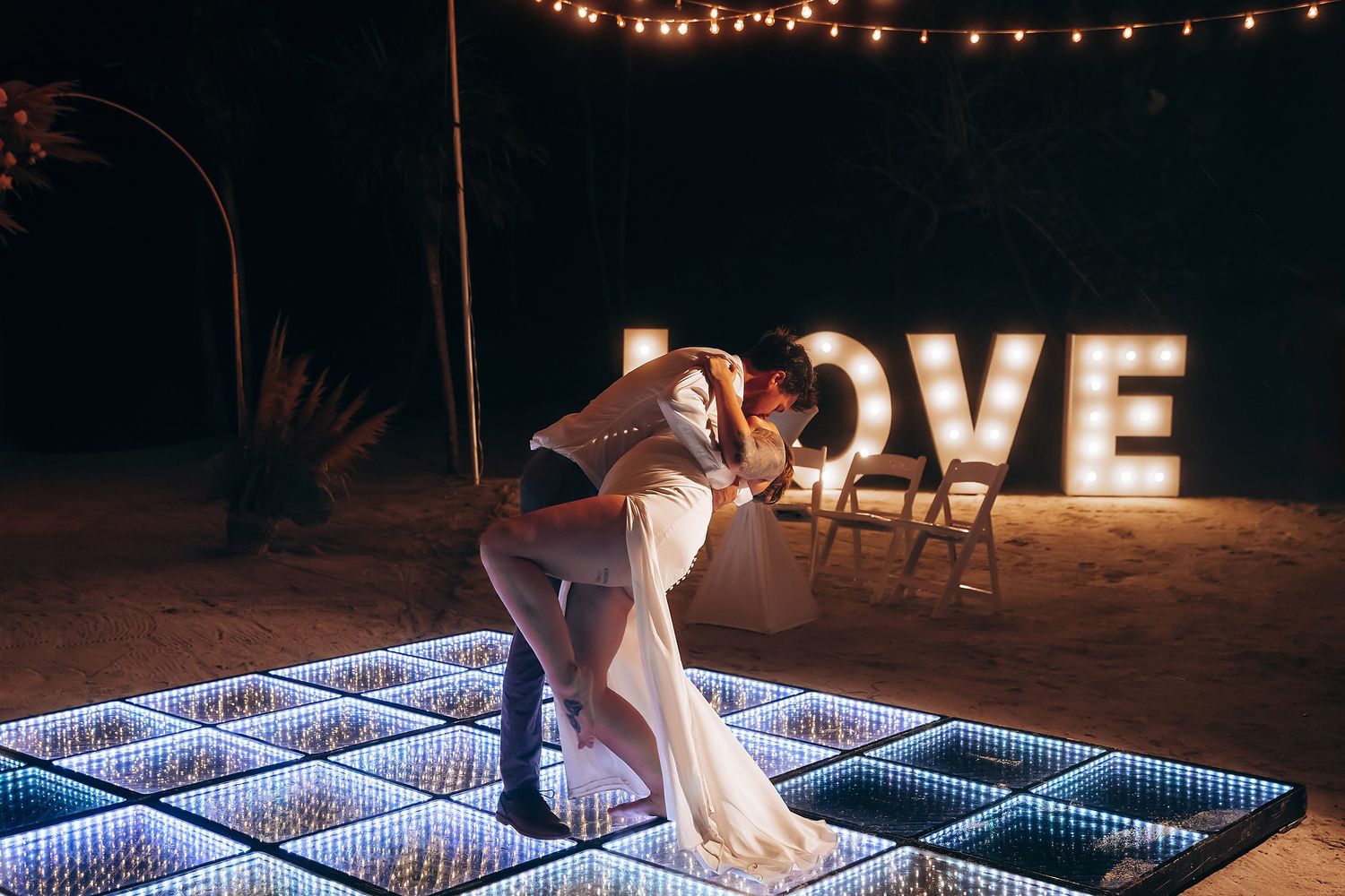 Wedding couple dances on an illuminated LED dance floor under string lights at night.