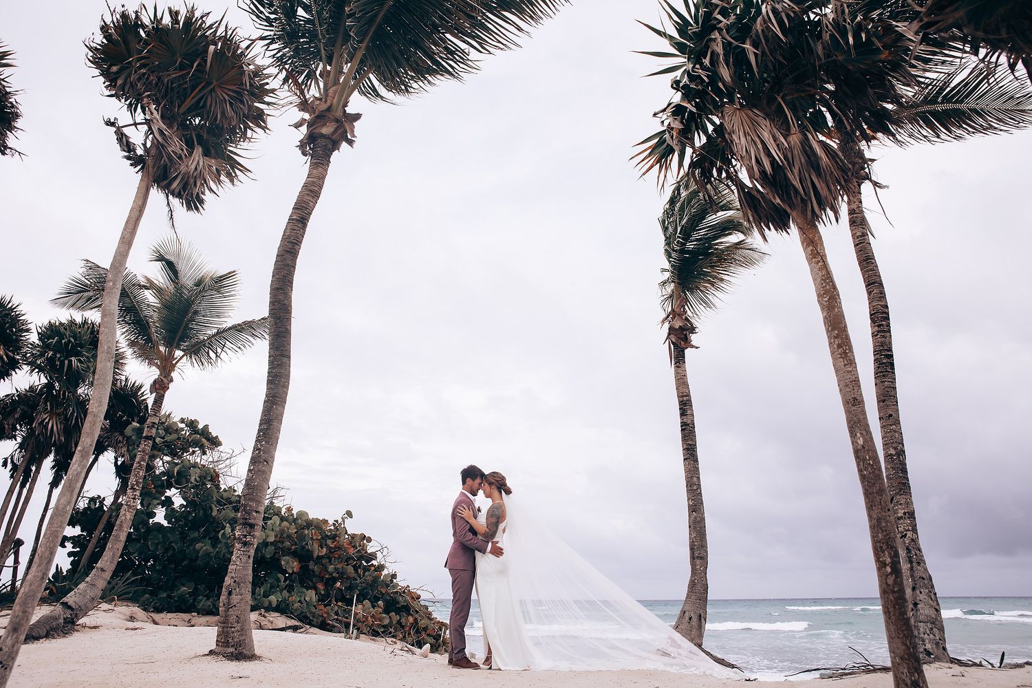 Palm trees sway against a cloudy sky at a coastal wedding venue.