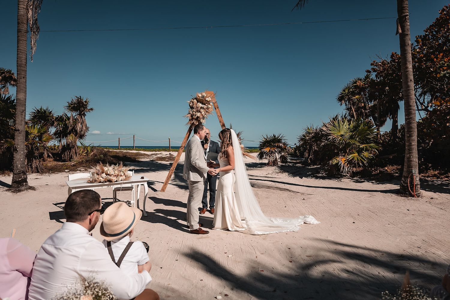 Wedding guests gathered along a palm-lined beach pathway during a tropical ceremony.