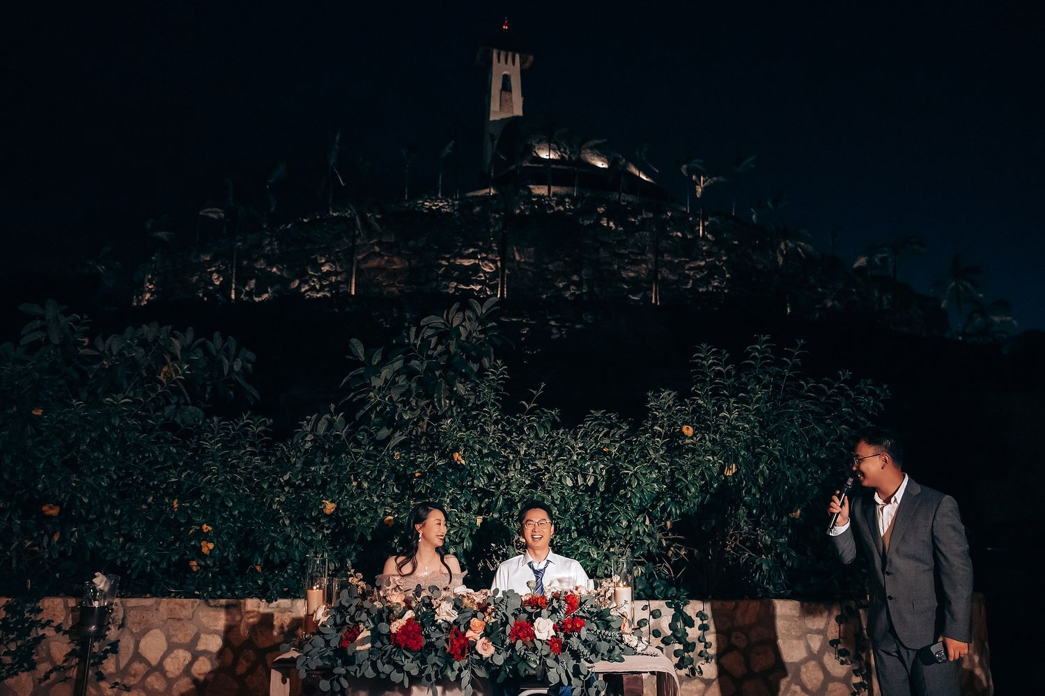 Wedding guests gather in a dimly lit outdoor garden venue with twinkling lights overhead.