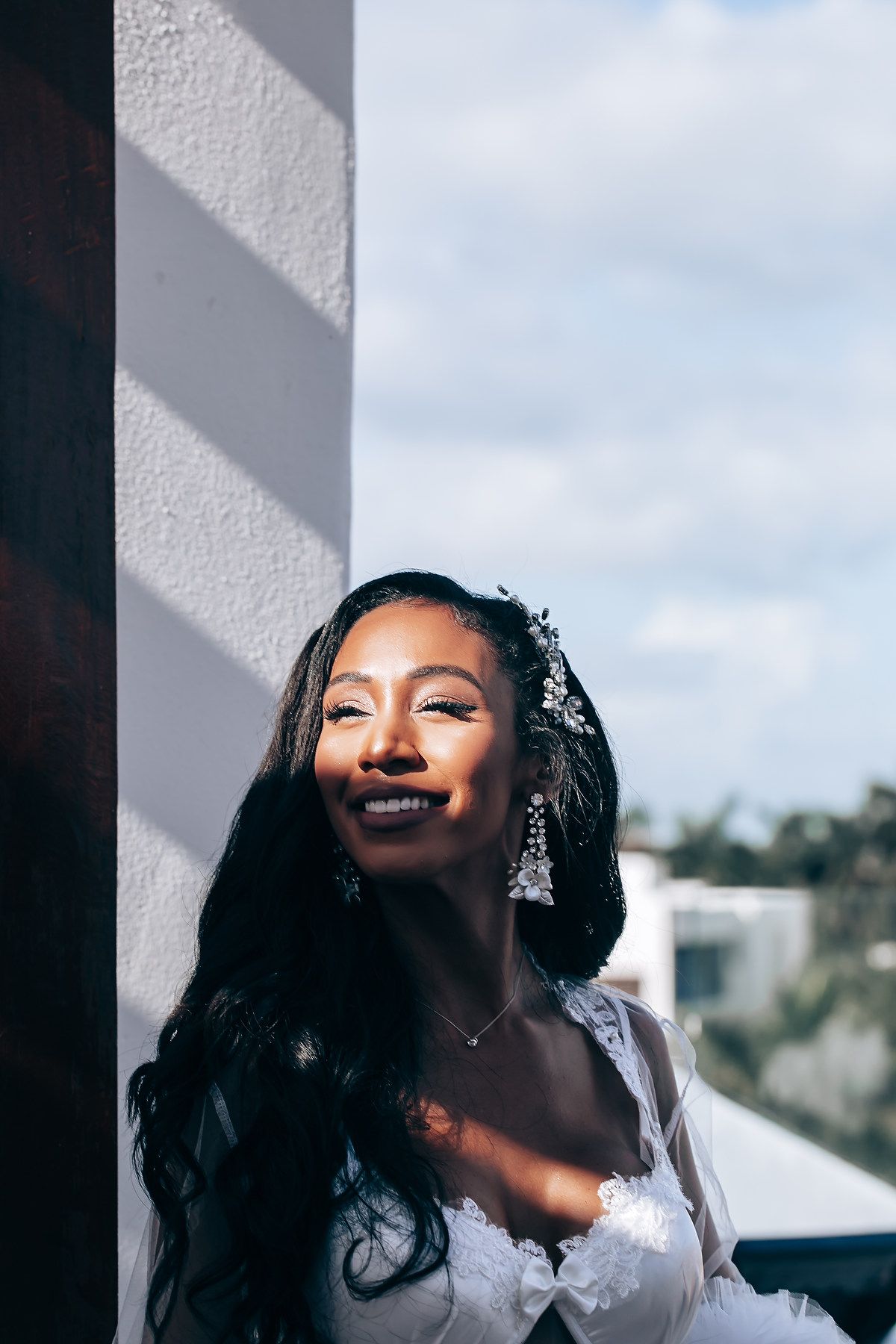 Sunlit bridal portrait with dramatic shadows and white dress against a cloudy sky.