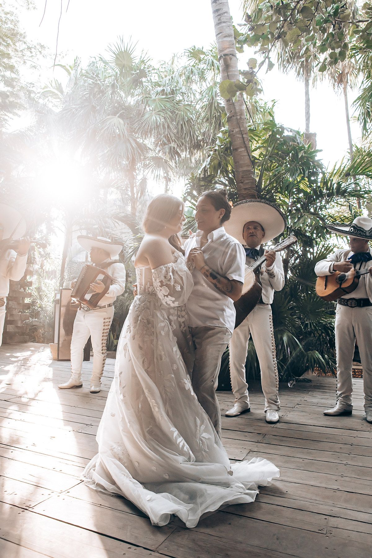 Couple dances together during a tropical outdoor celebration with palm trees and sunlight streaming through.