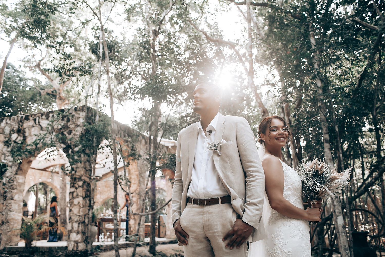 A couple shares a romantic moment under trees at their outdoor wedding ceremony.