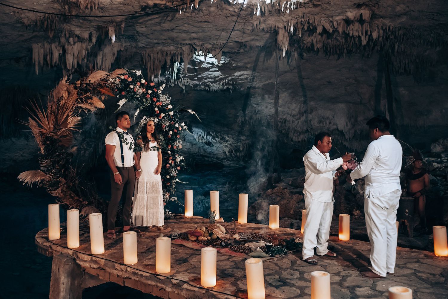 Illuminated candles line a dark pathway through trees creating a romantic outdoor wedding ceremony atmosphere.