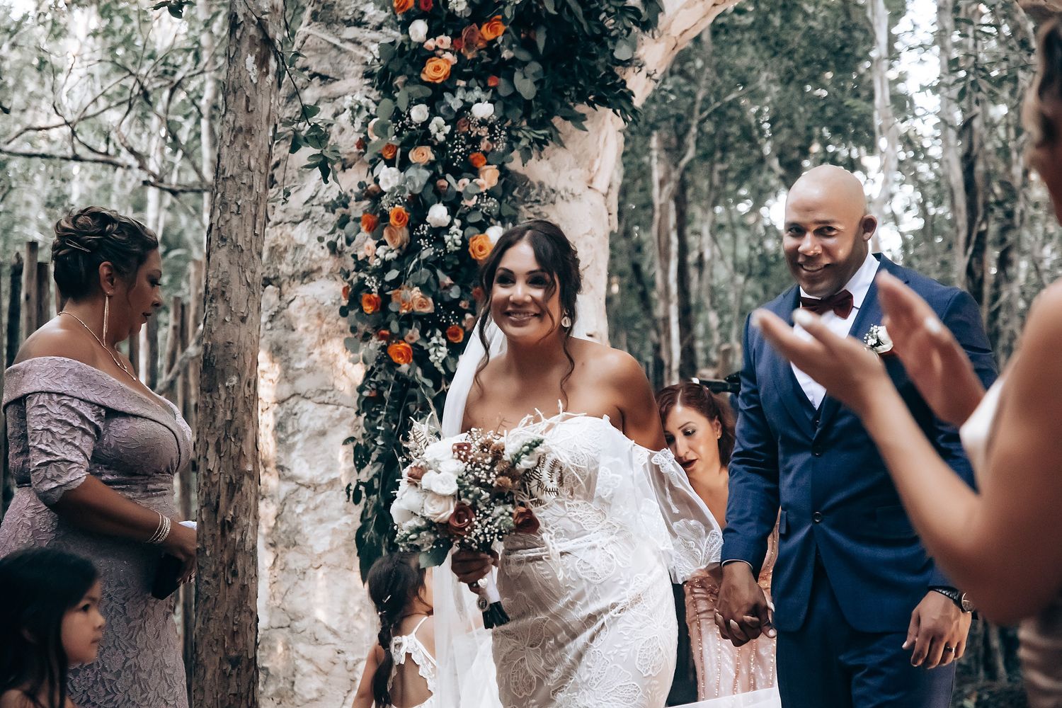 Wedding guests celebrating and dancing outdoors under trees decorated with string lights.