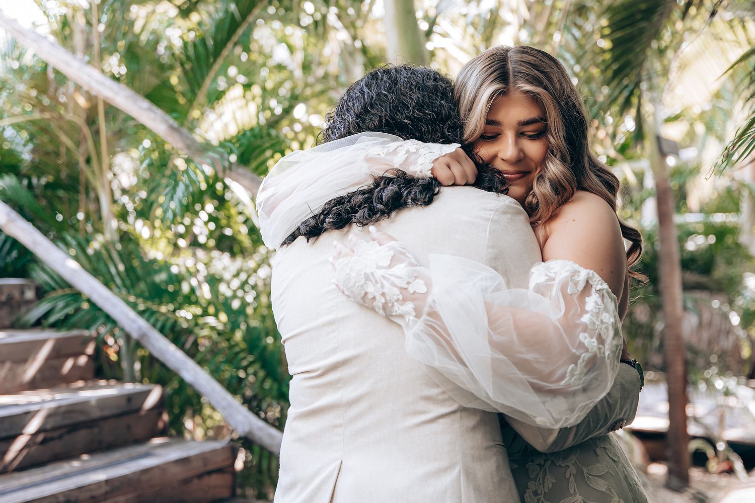 A couple embraces lovingly in a lush garden setting with natural sunlight filtering through the trees.