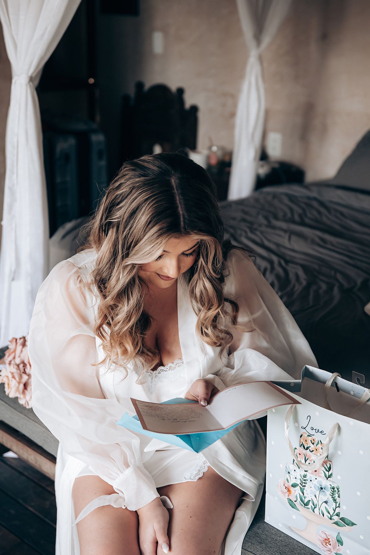 Artistic boudoir photography session featuring white lace robe and floral details in natural light.